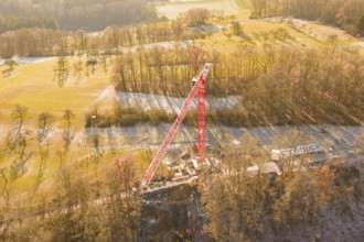 Crane dominates construction site in autumn landscape, surrounded by forests and meadows,