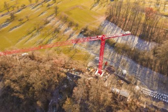 Red crane in the middle of a construction site, surrounded by autumnal landscape and meadows,