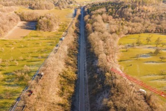 A railway cuts through fields and forests in a wintry countryside landscape, construction of the