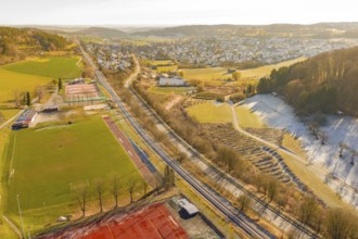 A railway traverses a scenic winter landscape with fields and a nearby village, construction of the