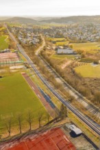 A railway line runs alongside fields and a sports complex near a village in winter, construction of