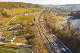 Aerial view of a railway running parallel to fields and a village nestled in a wintry landscape,