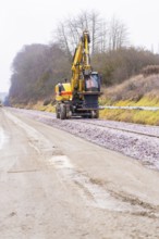 A yellow excavator works on a construction site along the tracks on a road, building the Hermann