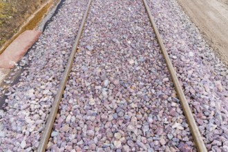 Close-up of railroad tracks covered with grey and purple gravel, construction of the Hermann Hesse