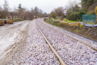 Railway tracks run curvy through a wooded landscape covered with gravel, construction of the