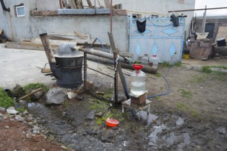 Self-built distillation plant in front of a rural farm with various materials, production of