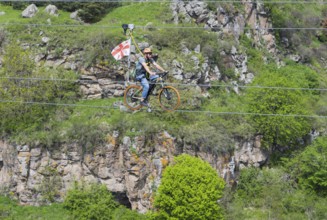 A person balances with a bicycle on a rope against a rocky backdrop, Dashbashi Gorge, Khrami River,
