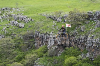 Person riding a bicycle on a stretched rope across a gorge in green countryside, Dashbashi Gorge,