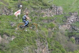 Man on a bicycle balancing at lofty heights above a green valley, Dashbashi Gorge, Khrami River,