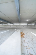 Empty parking lot with concrete floor, scattered leaves and parking space markings, parking garage
