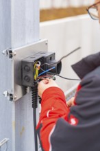 Person wearing a red jacket assembles electrical cables at a metal station, parking garage
