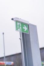 Green emergency exit sign with directional arrow on a metal post, parking garage construction with