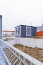 Shed on a fenced area with earthworks in the foreground, parking garage construction with charging