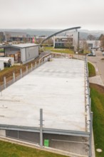 Aerial view of an empty parking lot with surrounding buildings and fences, parking garage
