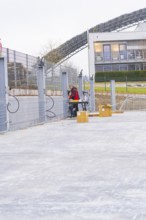 A worker sets up a table next to a fence with cables, boxes in the foreground, parking garage