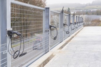 Cables run over a long fence on a concrete surface, with landscape in the background, parking