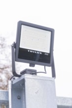 Close-up of a Trilux LED lamp on a post, with cloudy weather, parking garage construction with