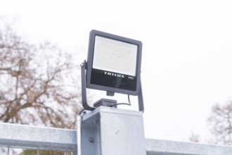 A Trilux LED lamp is mounted on a metal post, with cloudy sky, parking garage construction with