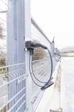 Cables are attached to a metal fence, with cloudy weather in the background, parking garage