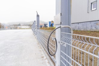 A cable is attached to a fence along a concrete surface. Industrial environment in the background,