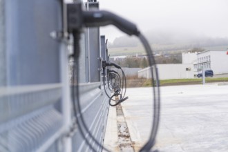 Cables run along a fence in an industrial environment with cloudy skies, parking garage