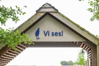 Welcome sign under a rustic wooden roof with green leaves, Vogelsee Tåkern, Vadstena,