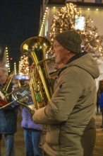 Tuba player in winter clothes on a street decorated with lights, Weihnachtsmark Nagold,