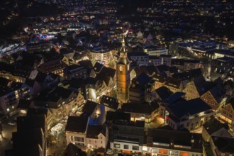 Illuminated church tower in the middle of a nocturnal urban landscape with surrounding buildings,