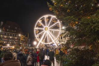 Illuminated Ferris wheel and half-timbered houses at night on a busy Christmas market,