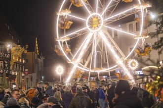 Large illuminated Ferris wheel next to a crowd at a Christmas market at night, Weihnachtsmark