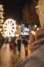 A person photographs a glowing Ferris wheel at a Christmas market, Weihnachtsmark Nagold,