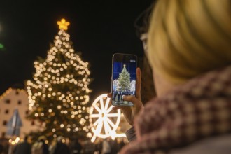 A person photographs a festively illuminated Christmas tree at night, Weihnachtsmark Nagold,