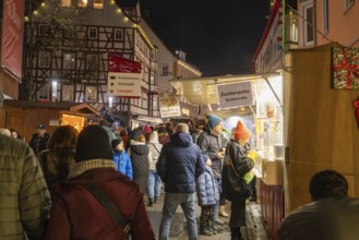 Visitors stand at an illuminated stand at a night market, half-timbered buildings in the