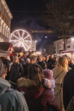 Visitors at a busy night market with illuminated Ferris wheel in the background, Weihnachtsmark