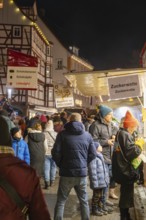 Night market visitors at an illuminated cotton candy stand in front of half-timbered houses,