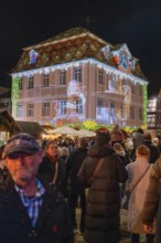 People in a festive square at night with an artistic light show on a building, Weihnachtsmark
