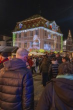 People at a Christmas market in front of an illuminated historic building with a projection,