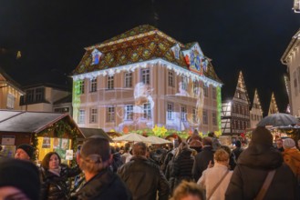 Lively scene at a market with light projection onto a building and people celebrating,