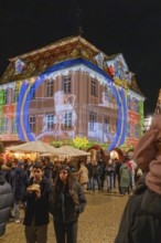Artistic light projection onto a building at night, surrounded by people and a festive atmosphere,