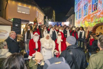 People wearing Christmas costumes at a night outdoor party surrounded by colorful lights,