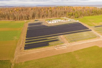 Aerial view of a solar park surrounded by fields and autumn forest, energy revolution, construction