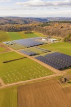 Aerial view of a solar park surrounded by fields and autumn forests, energy revolution,