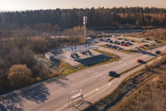 Wide angle view of a street with cars and a charging station, surrounded by autumn trees and