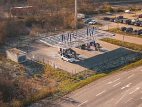 Electric car at a charging station under a solar roof, surrounded by autumn trees and cars in a
