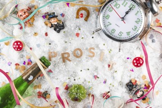 Letters cheers in the snow surrounded by lucky charms, watch and champagne bottle, New Year's Eve