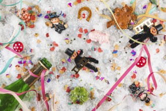 Various lucky charms, champagne bottle and confetti on snow, New Year's Eve
