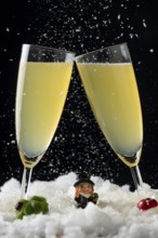 Snow falls on two champagne glasses in snow with lucky New Year's Day charms