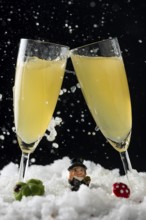 Two sparkling champagne glasses in the snow with lucky New Year's Day charms