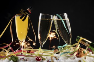 Three champagne glasses with lucky New Year's Day charms, streamers and sparklers in the snow