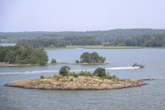 Small, wooded island in calm water with passing patrol boat boat, marine speedboat, Aaland Islands,